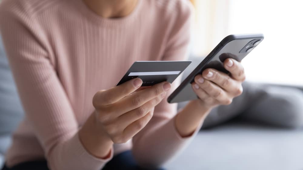 Mujer sosteniendo su tarjeta de débito y teléfono inteligente para verificar su transferencia de sobregiro en línea