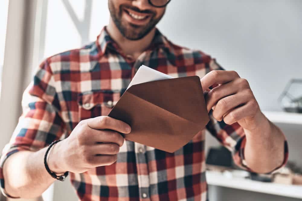 Hombre quitando un certificado de regalo imprimible de un sobre marrón