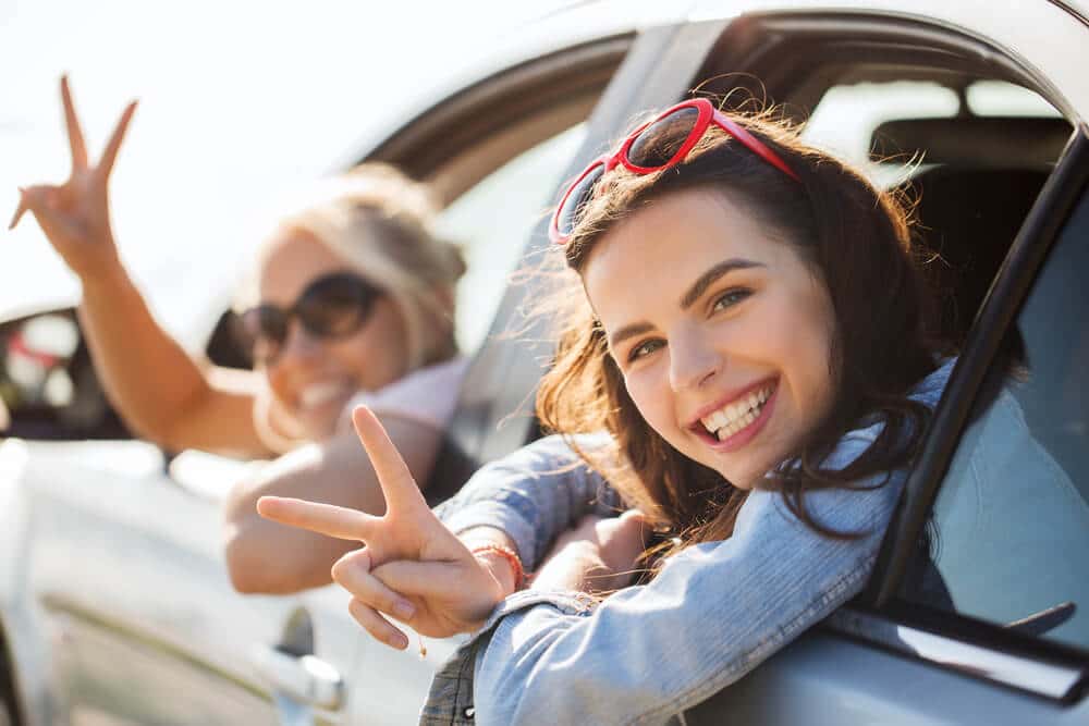 Sonríen dos mujeres de 18 años que están a punto de irse en su coche de alquiler.