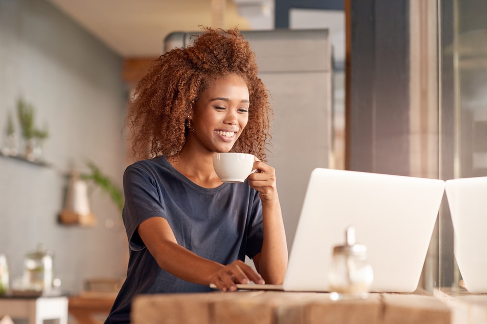 Mujer navegando por un sitio de compras FlexPay en su computadora portátil mientras bebe café