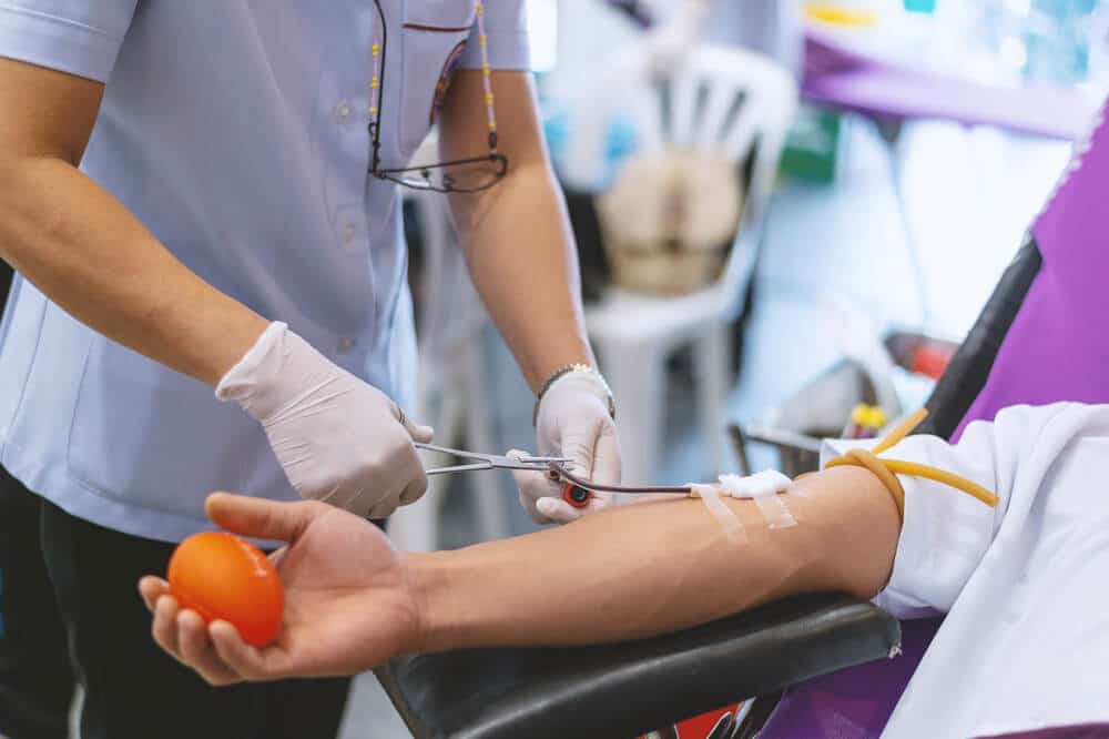 Mujer ajustando el tubo en el brazo del donante mientras el donante se prepara para donar sangre o plasma