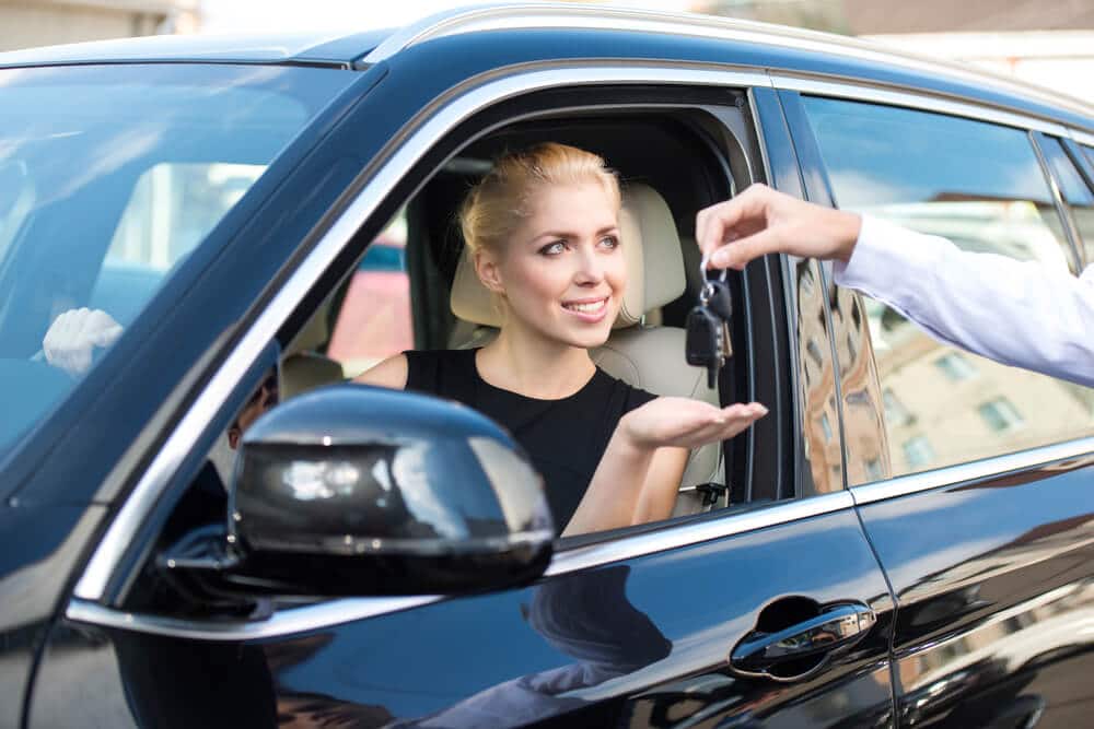 mujer en el asiento del conductor al que le entregan las llaves de su coche de alquiler