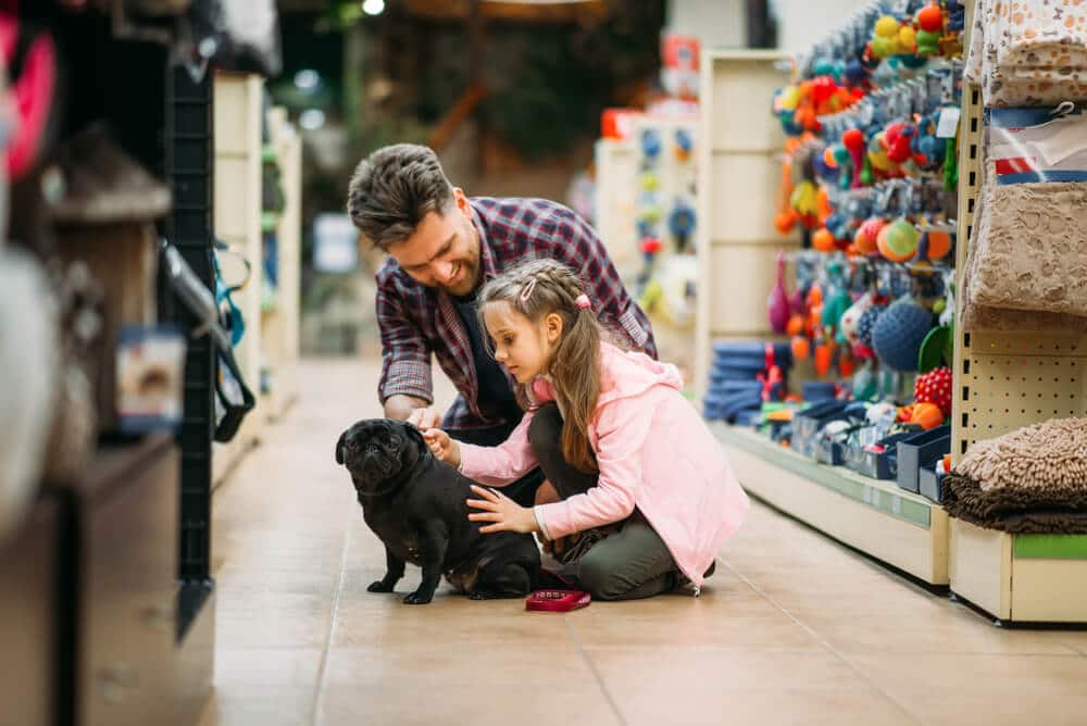 Padre e hija con perro negro en el pasillo de la tienda de mascotas