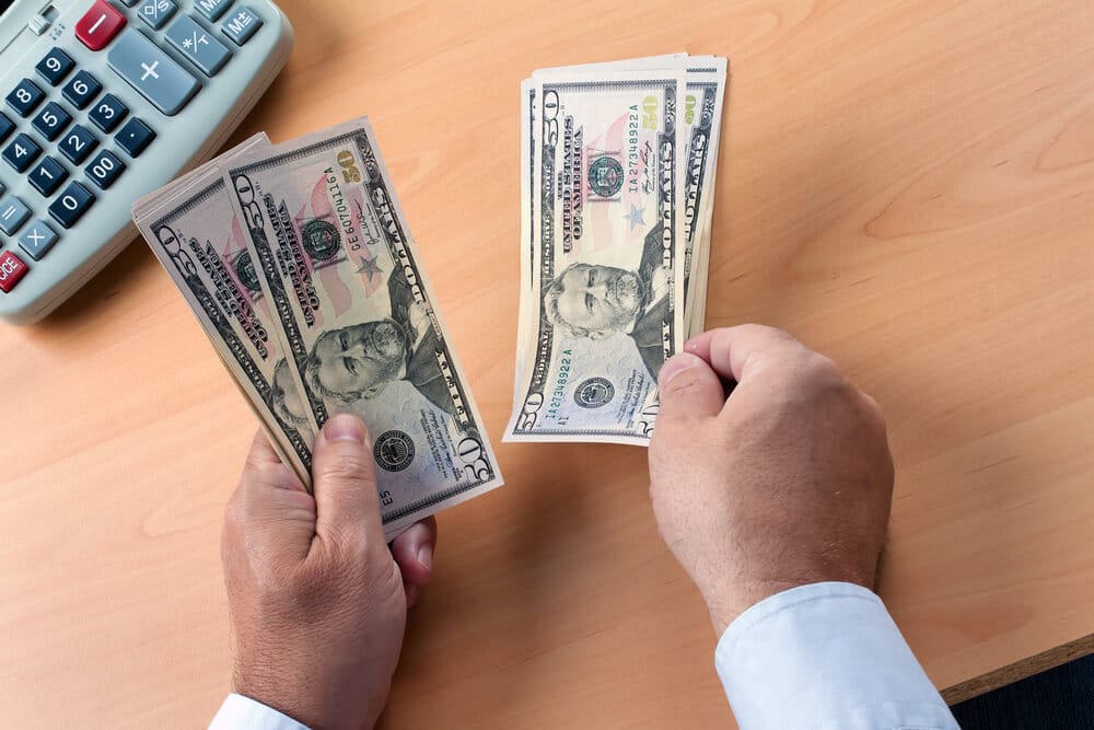 Un hombre tiene billetes de $50 cerca de una calculadora en un escritorio